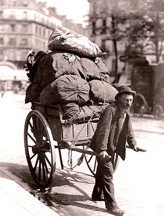 Ett svartvitt foto av en man som drar ett stort lass med säckar.