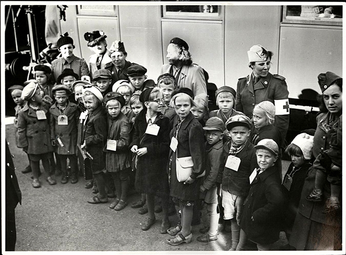 En grupp barn står vid en tågvagn, alla har namnlapp runt halsen