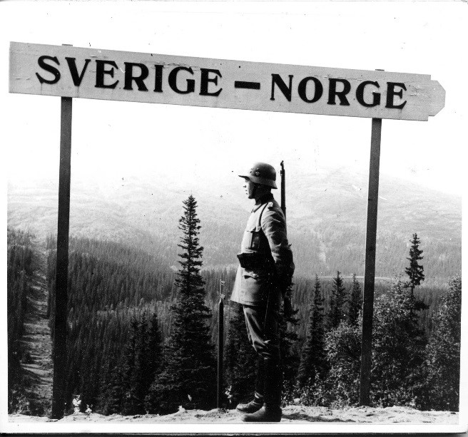 En man i uniform står vid en skylt med texten Sverige - Norge