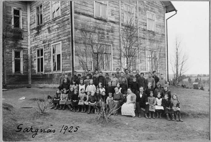 En grupp barn och lärare utanför en stor träbyggnad
