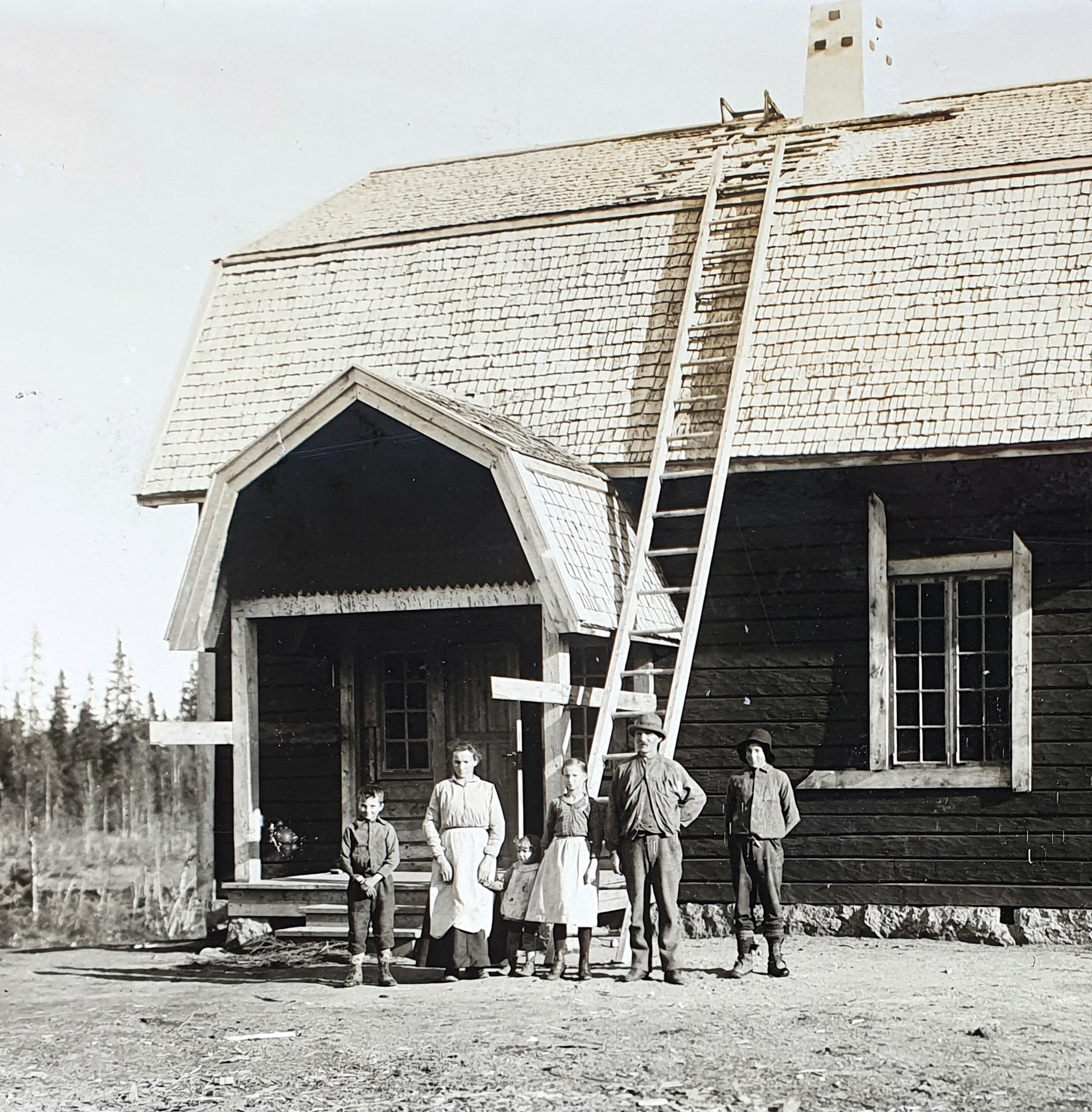 Äldre svartvitt foto föreställandes en familj utan för ett hus