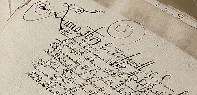 Närbild av ett gammalt handskrivet dokument med detaljerad kalligrafi. Ett stort dekorativt ”Anno 1679” högst upp och kursiv text nedanför.