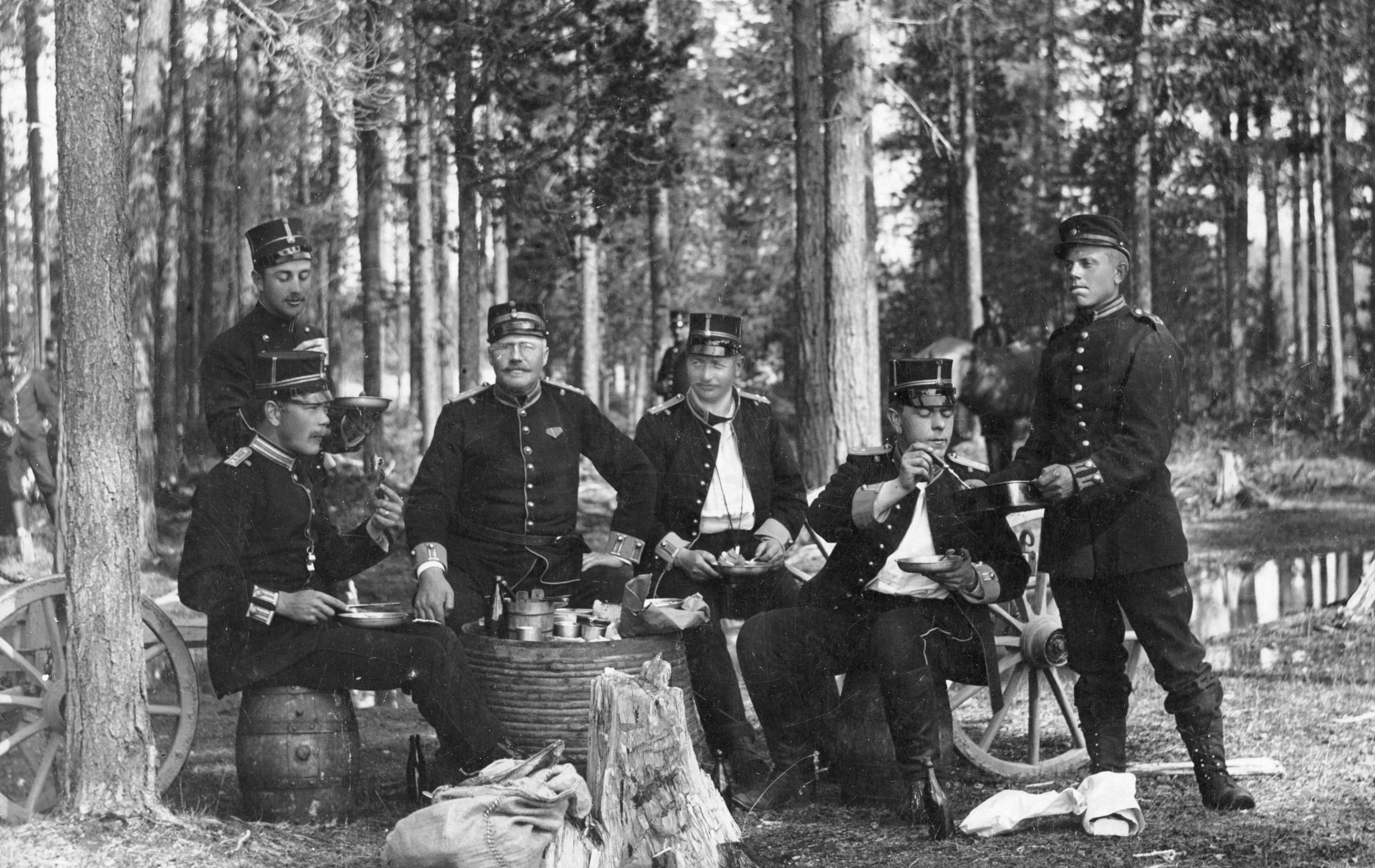 En grupp soldater från ett äldre regemente sitter och äter ute i en skogsmiljö, klädda i uniformer från 1800-talet