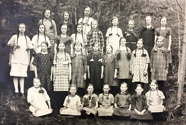 En gruppbild i svartvitt där en klassuppsättning flickor har flätor