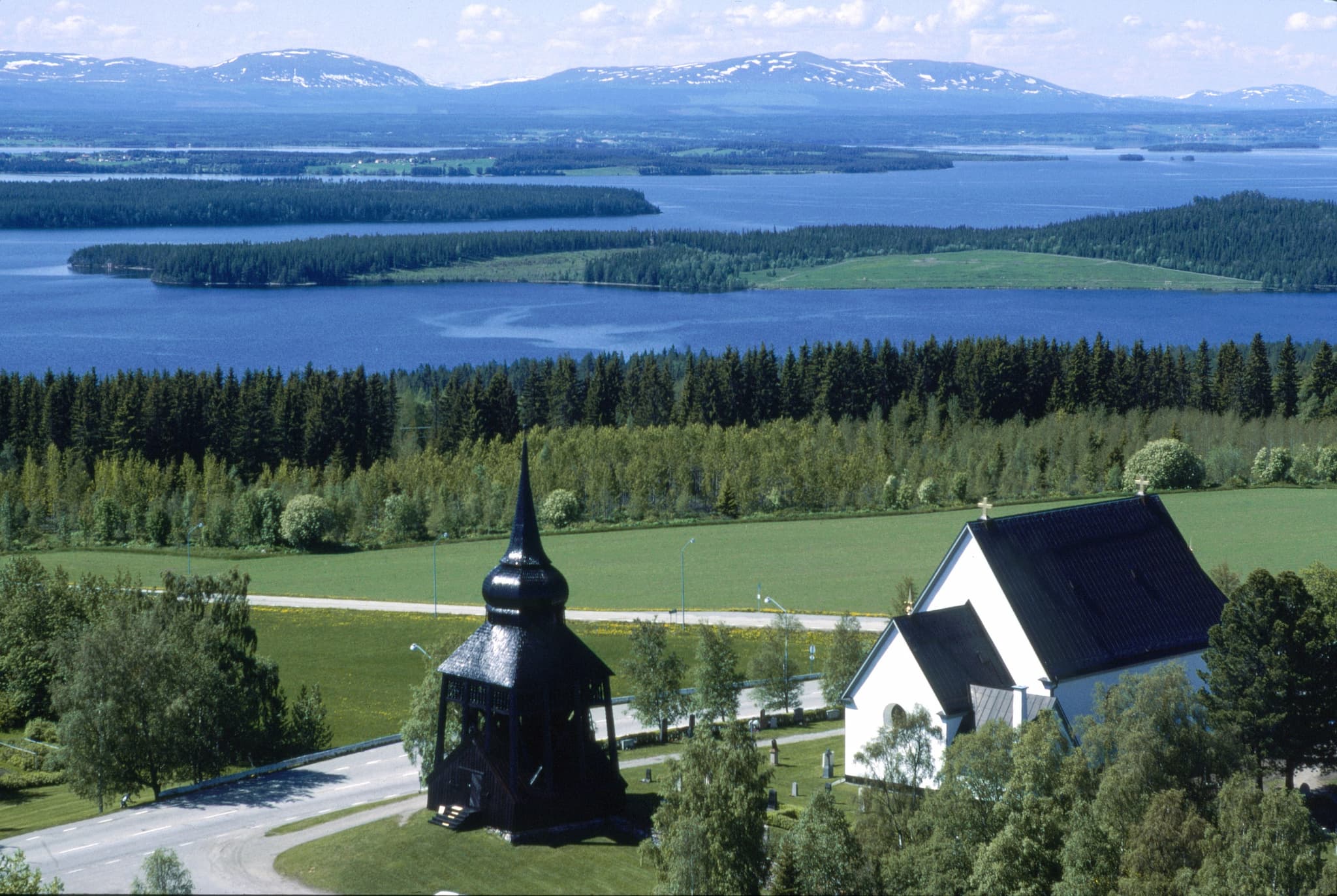 Foto av Frösö kyrka taget uppifrån. I bakgrunden ser man storsjön och fjäll.