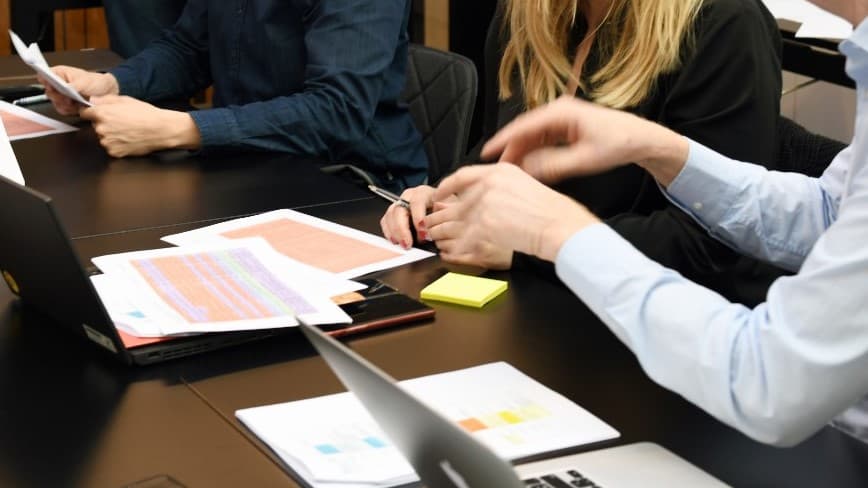 Ett bord med papper och datorer och några personers händer