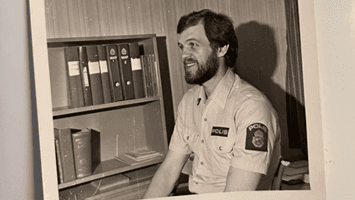 En person med en polisskjorta sitter vid en bokhylla.