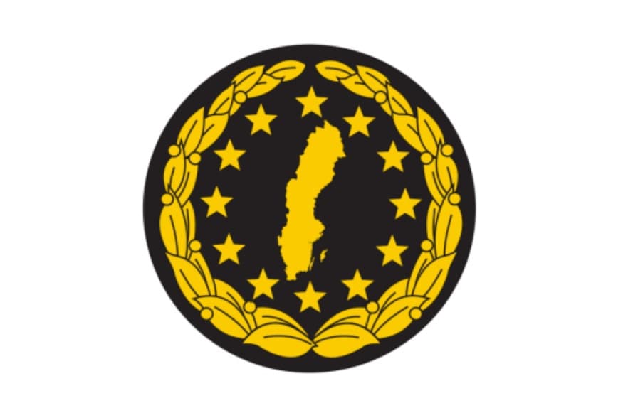 Ett märke med guldkrans, guldstjärnor och sveriges karta i guld. På svart botten.