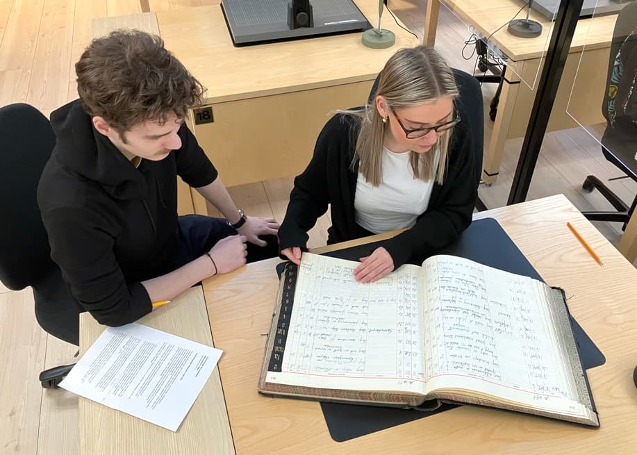 Två personer vid bord med bok uppslagen.