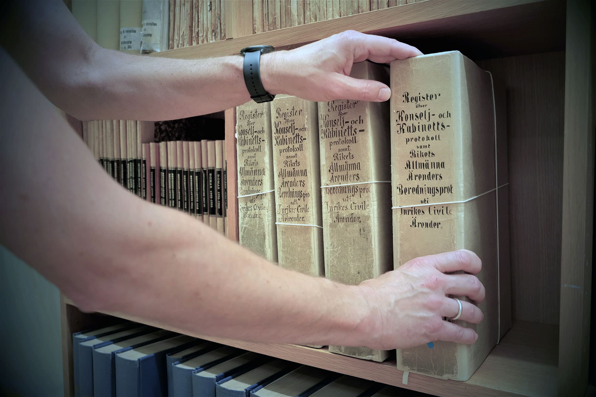 Två händer som rör vid äldre arkivhandlingar.