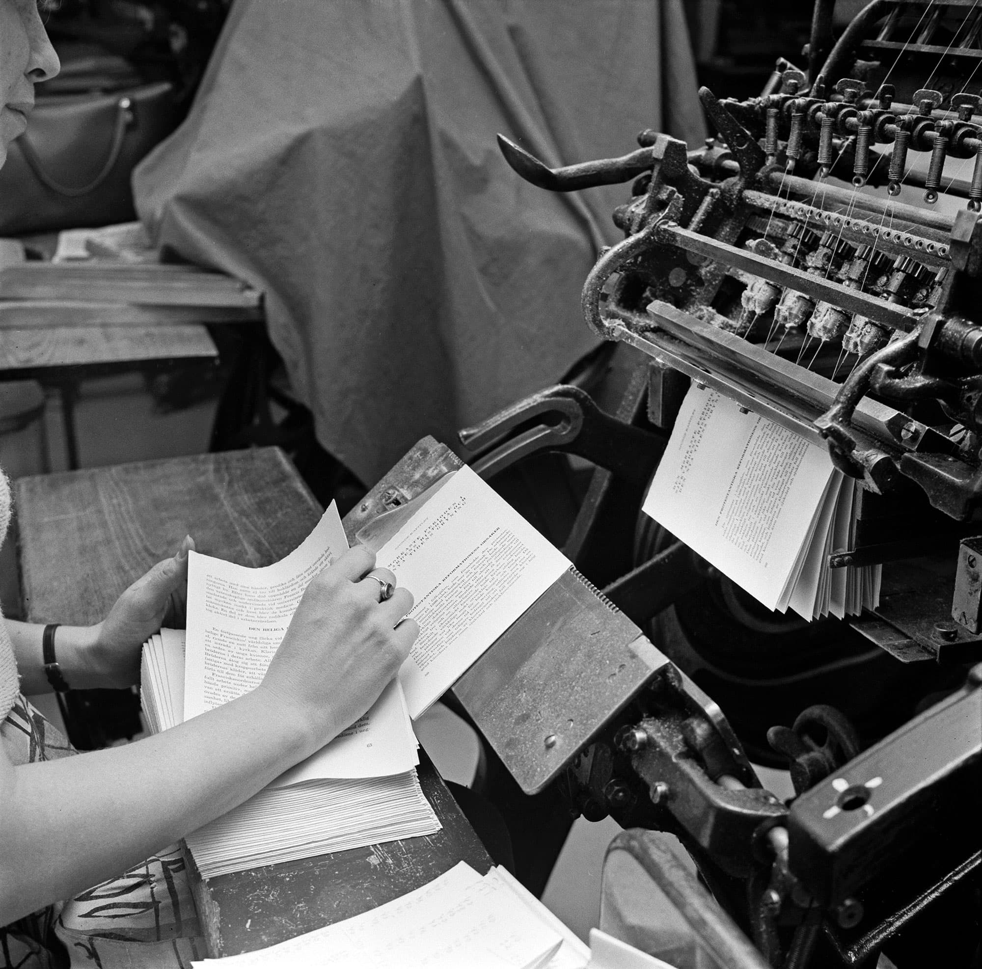 Händer vid ett bord som bläddrar i sidor från en tryckpress.