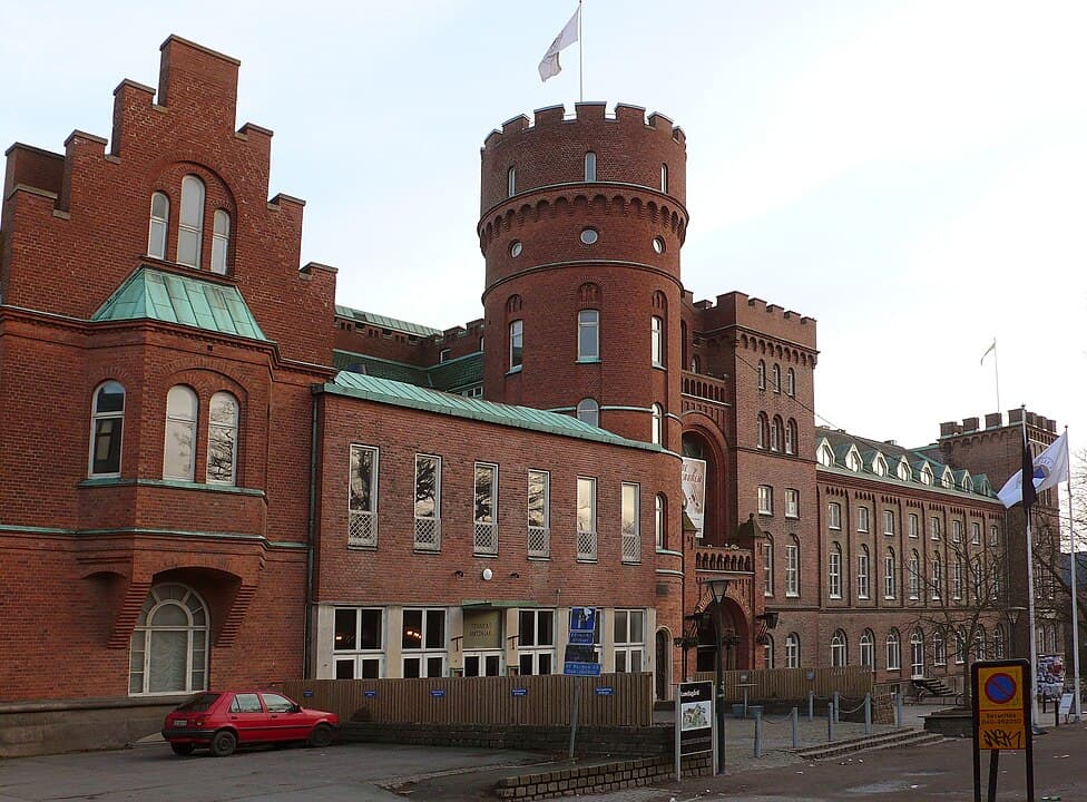 En stor röd tegelbyggnad med torn och grönt tak.
