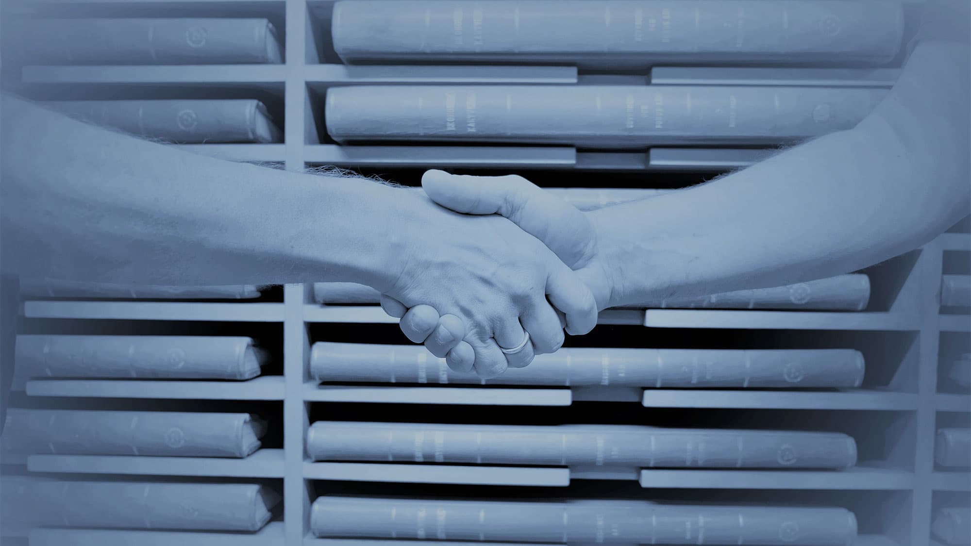 Två personer skakar hand framför hyllor med dokument.