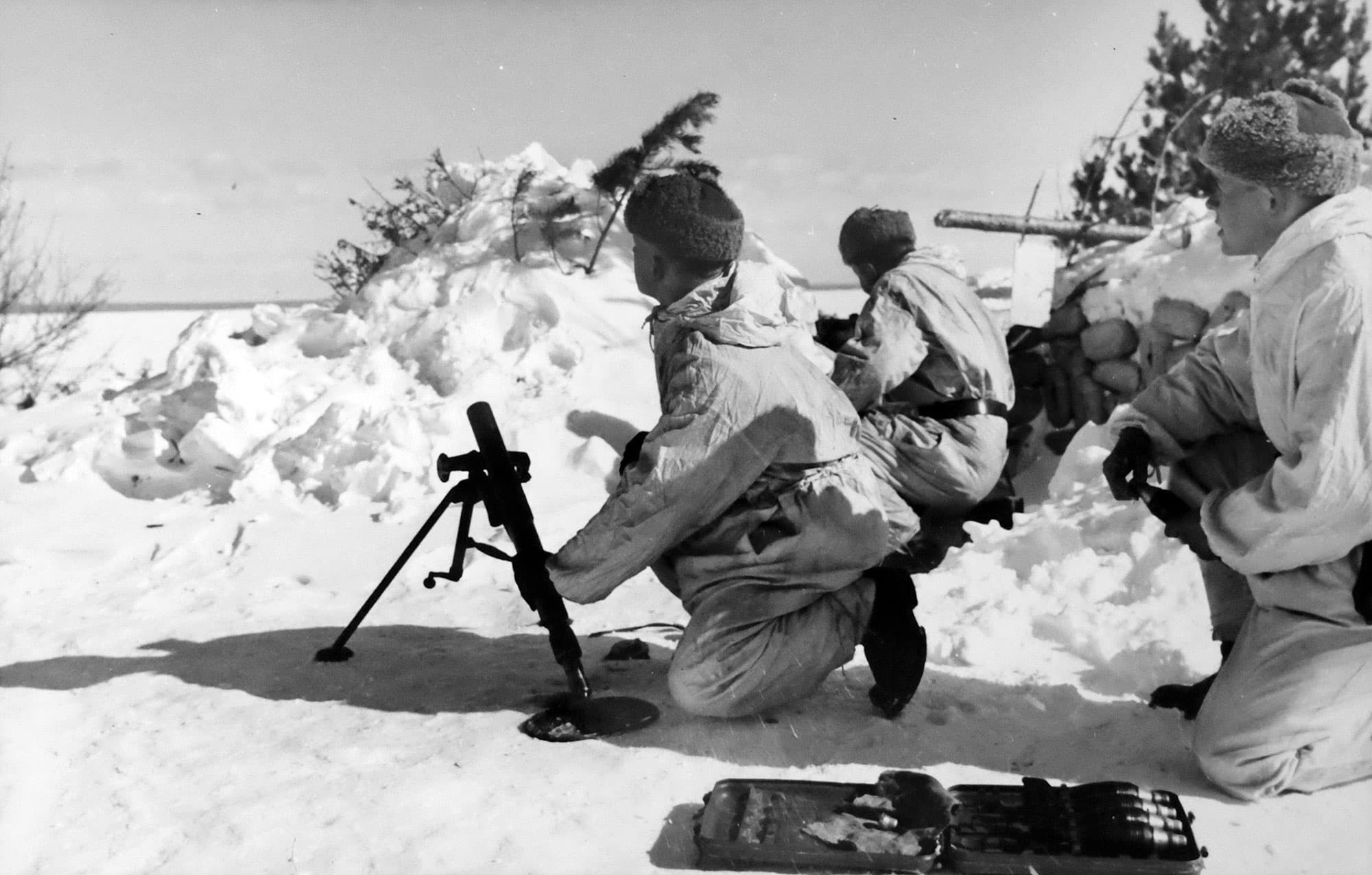 Tre soldater i vinterkamouflage hanterar en granatkastare i snölandskap under militär operation eller övning.