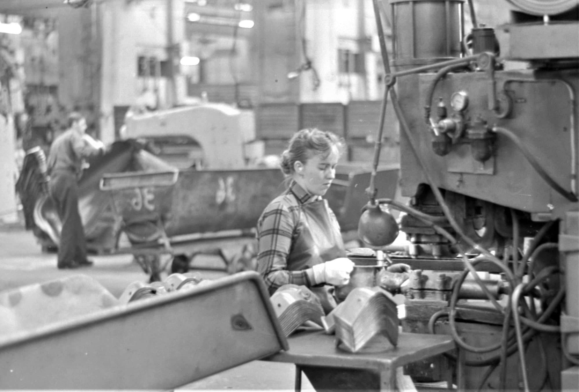 Kvinna framför maskin i fabrik.