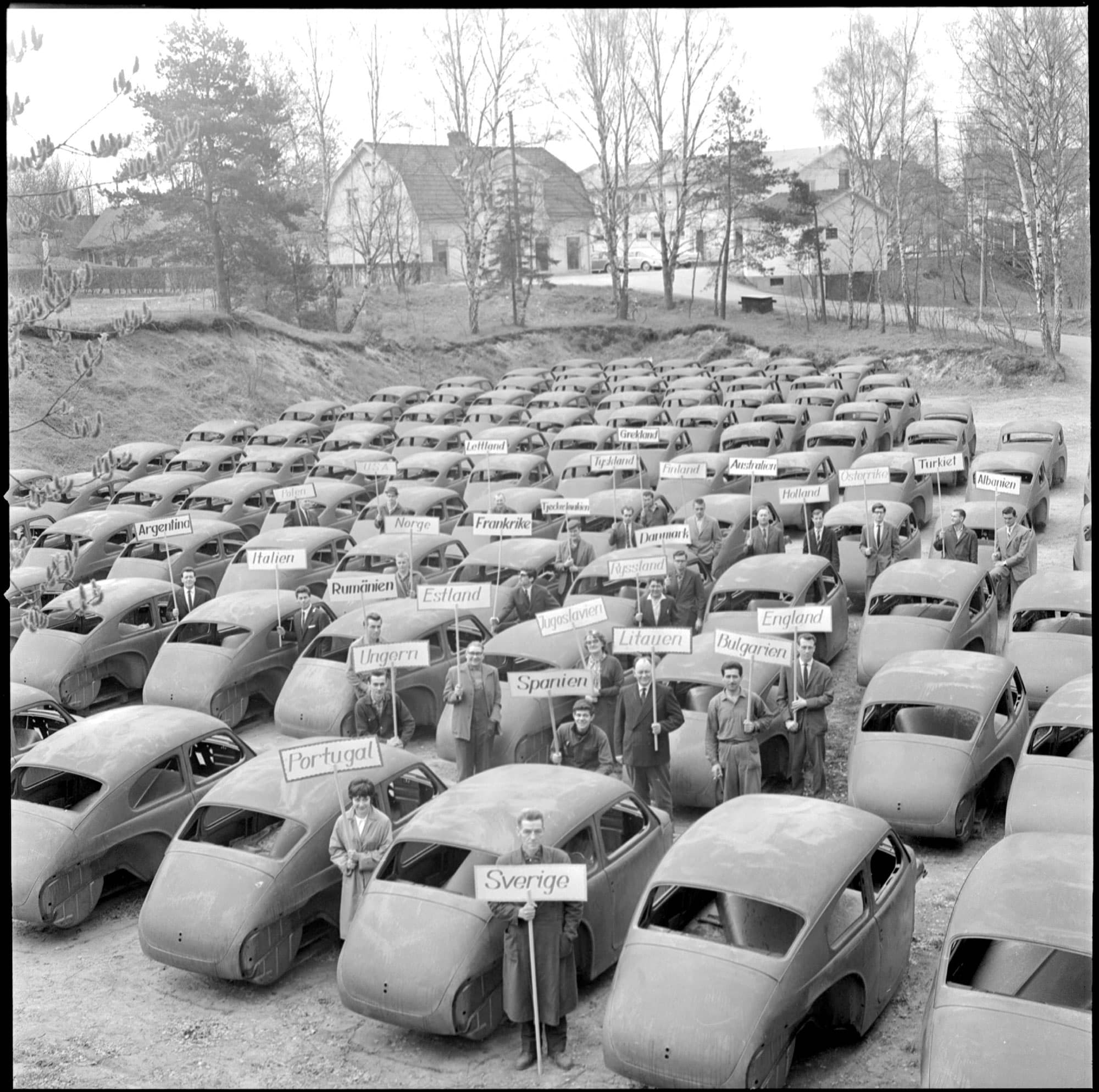 Parkering med bilar där människor håller upp skyltar med olika länders namn.