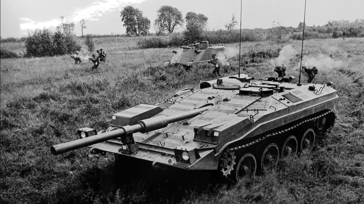 Stridsfordon och soldater i fält under militär övning eller insats.