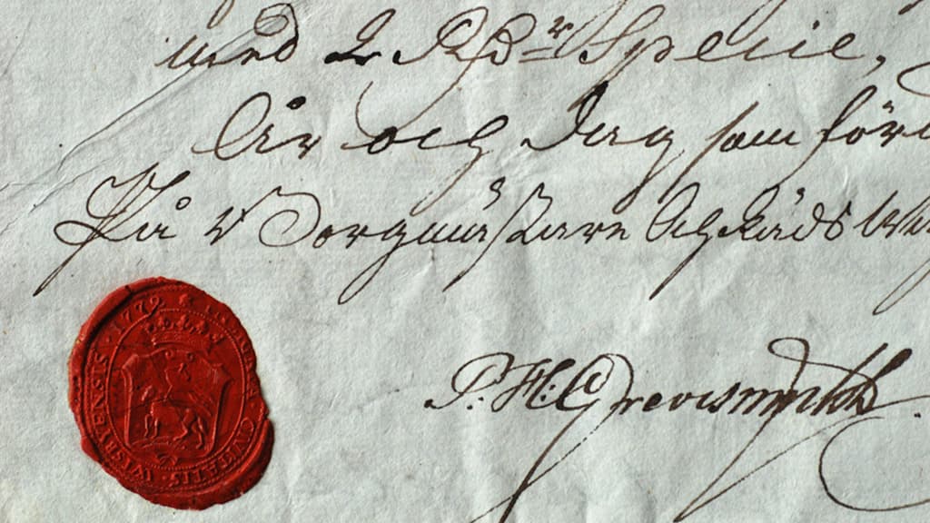 Närbild av ett dokument med sirlig handskrift och ett rött sigill i nederkant.