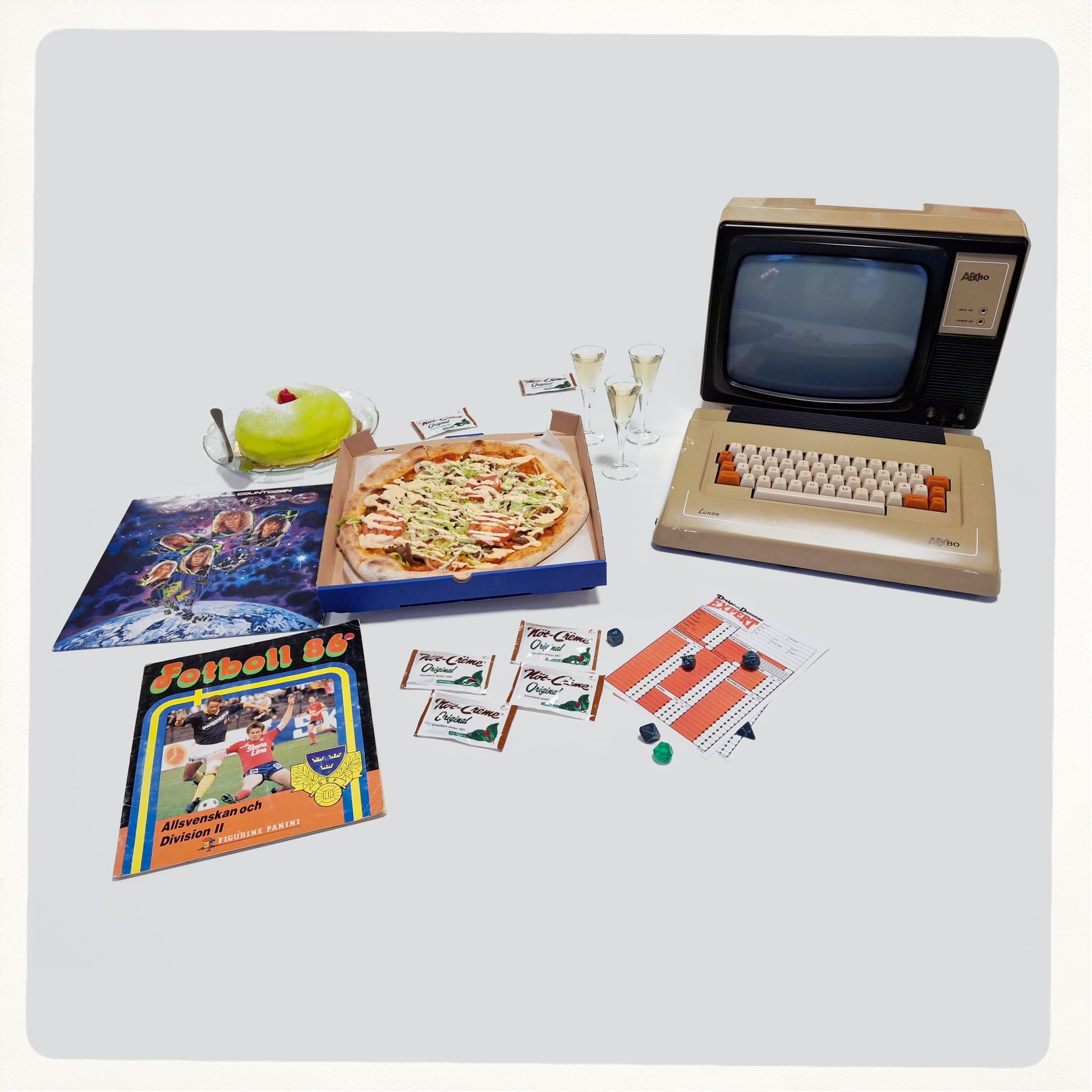 En tidig dator, en pizza, en prinsesstårta, ett skivomslag mm. mot vit bakgrund.