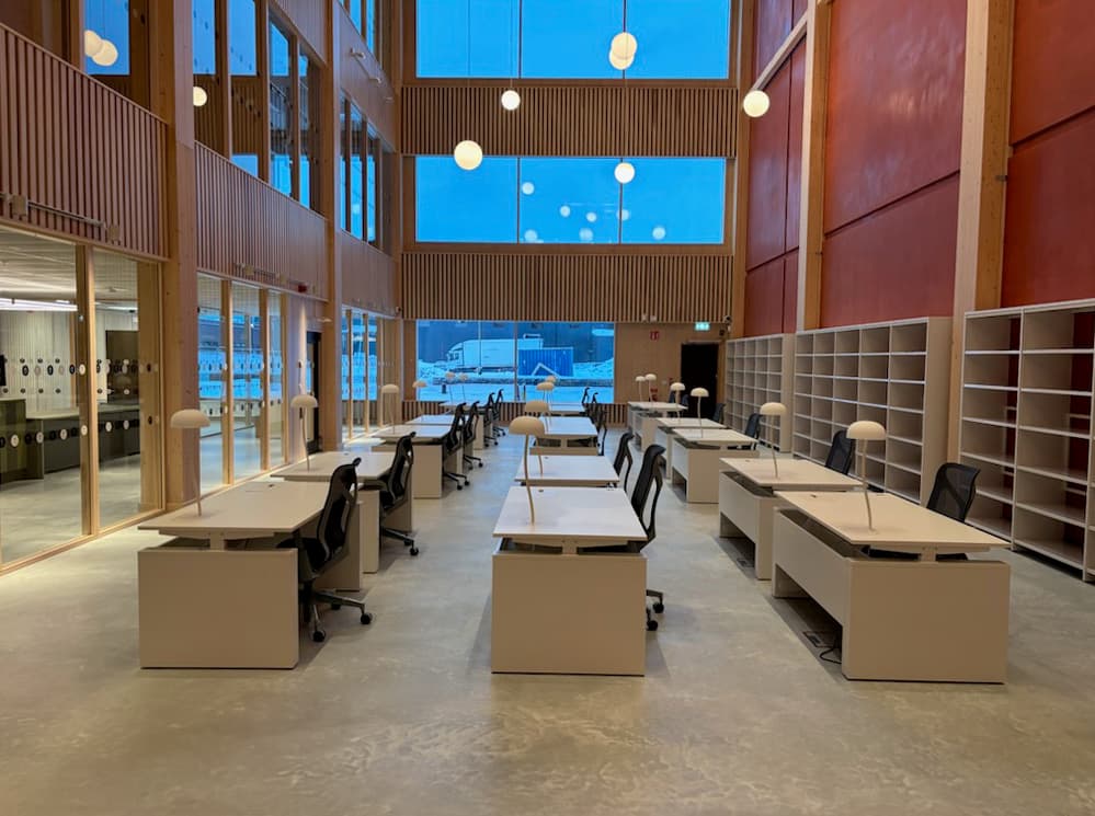 Tre rader av tomma bord i ett rum med röda väggar. Till höger står en tom bokhylla.