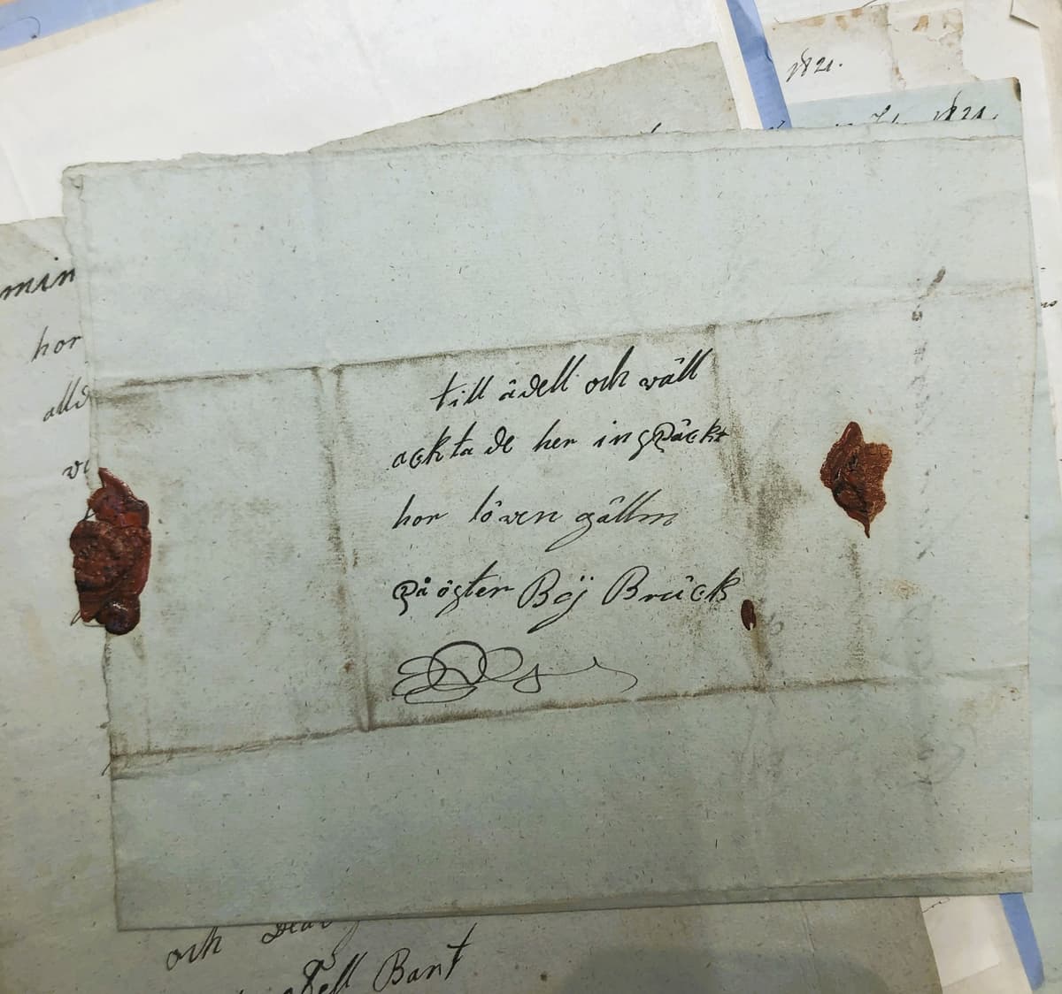 Ett gammalt handskrivet brev med röd lacksigill, omgivet av andra åldrade dokument.