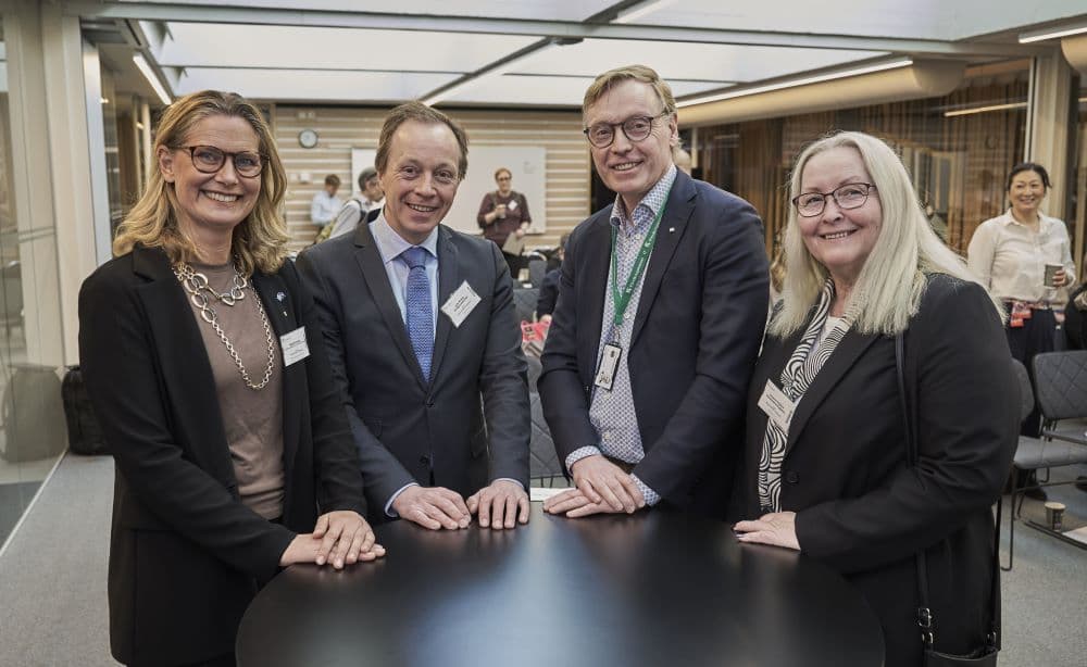 fyra personer står vid runt bord i konferenslokal.