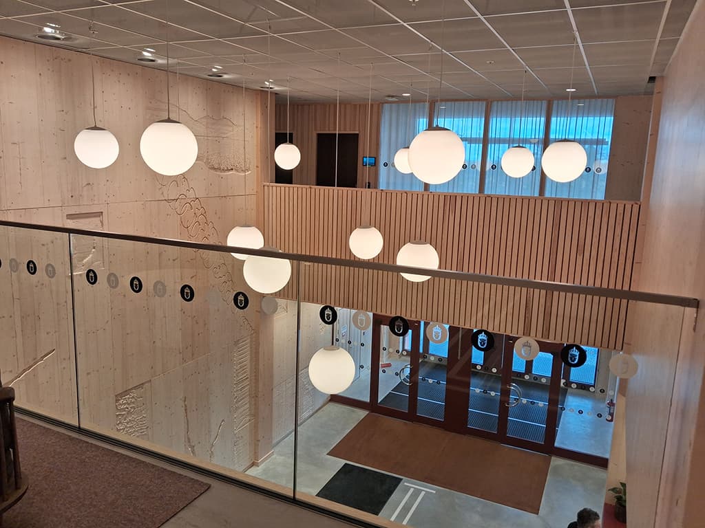 En ljus entré med träväggar, stora runda lampor i taket och glasdörrar som leder ut.