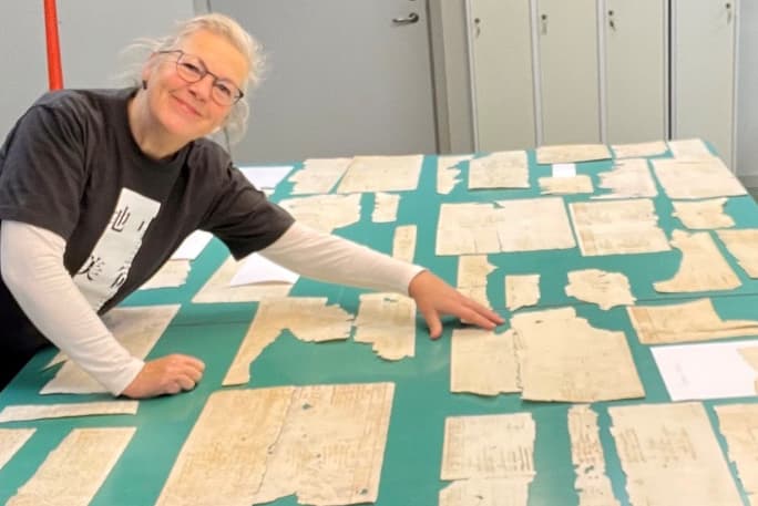 Person vid ett bord fyllt av fragment av gamla dokument.