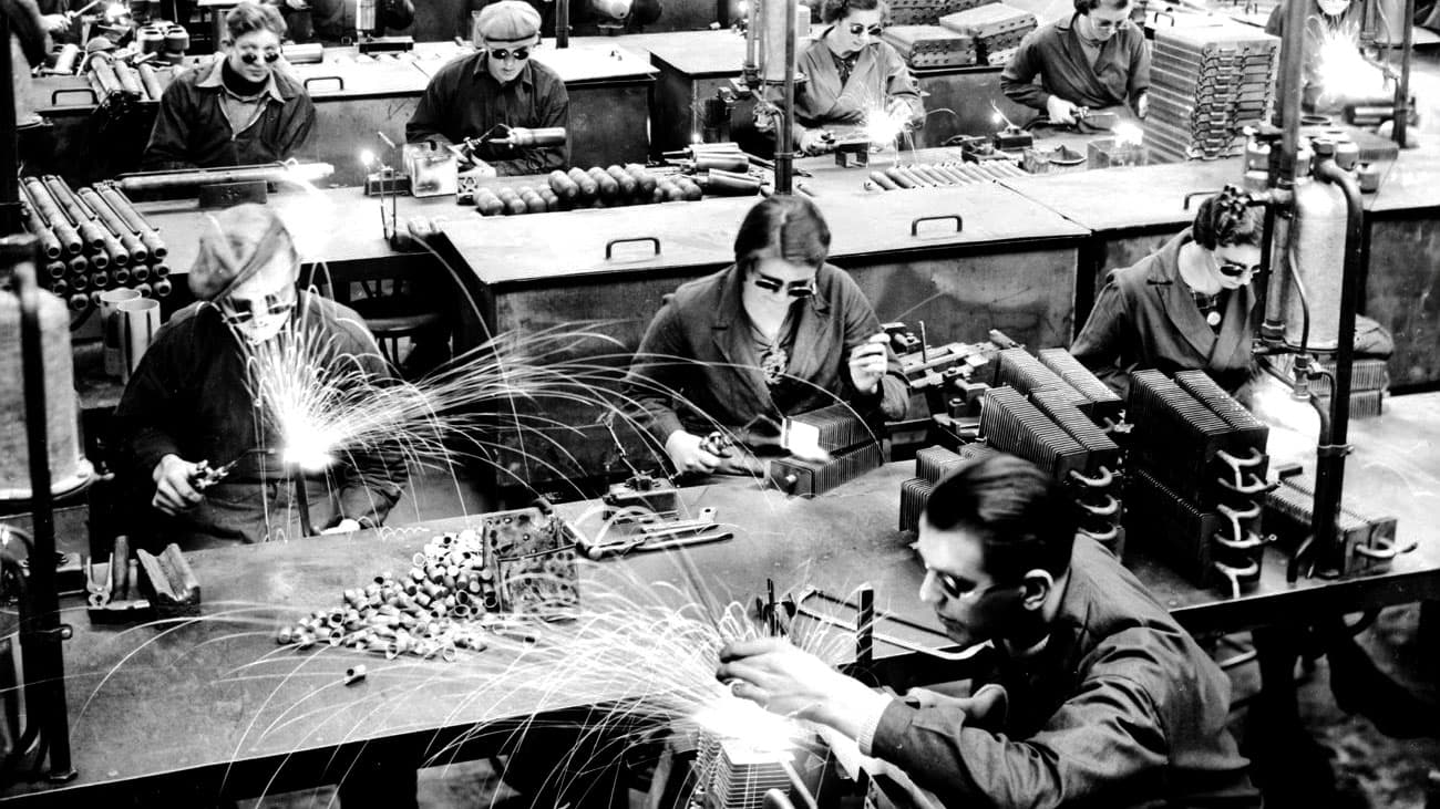 Arbetare svetsar och slipar metall i fabrik, gnistor flyger.