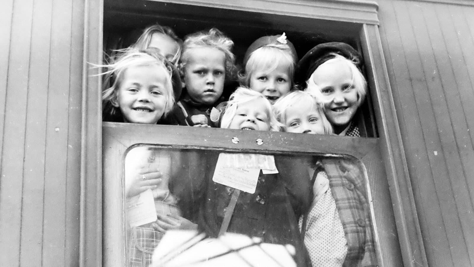 Svartvit bild på barn som tittar ut genom ett tågfönster.