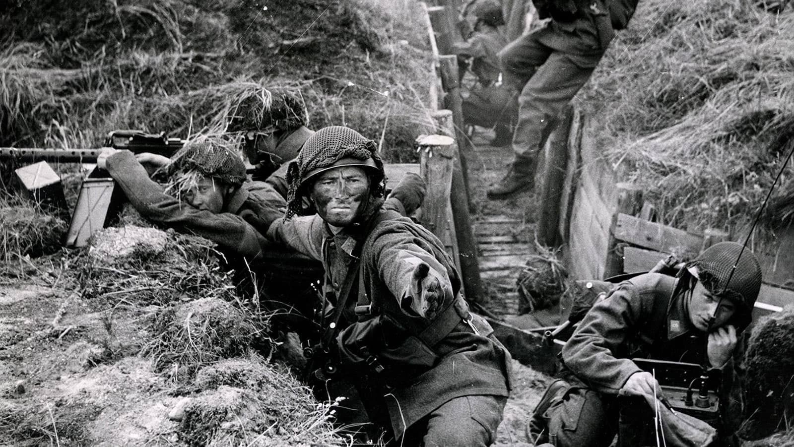 Soldater i skyttegrav under strid, en pekar framåt i ett intensivt ögonblick.