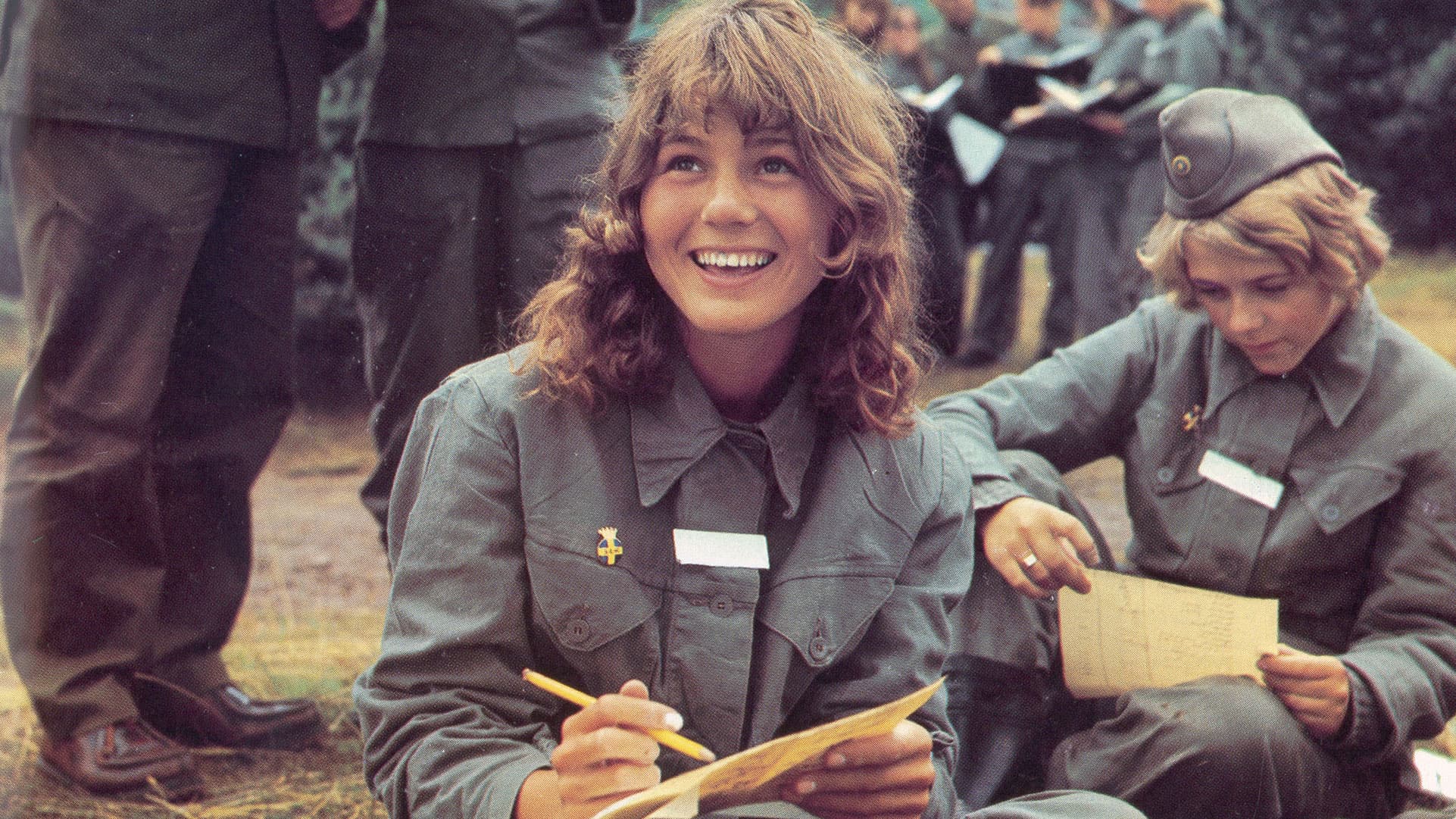 Ungdomar i uniform deltar i utbildning, två sitter och skriver med glada uttryck.