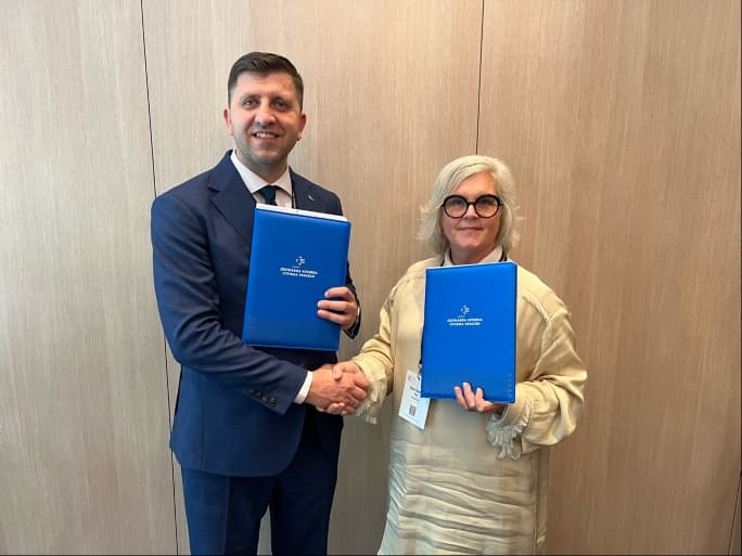 Två personer skakar hand och håller varsin blå mapp efter undertecknandet av ett samarbetsavtal.