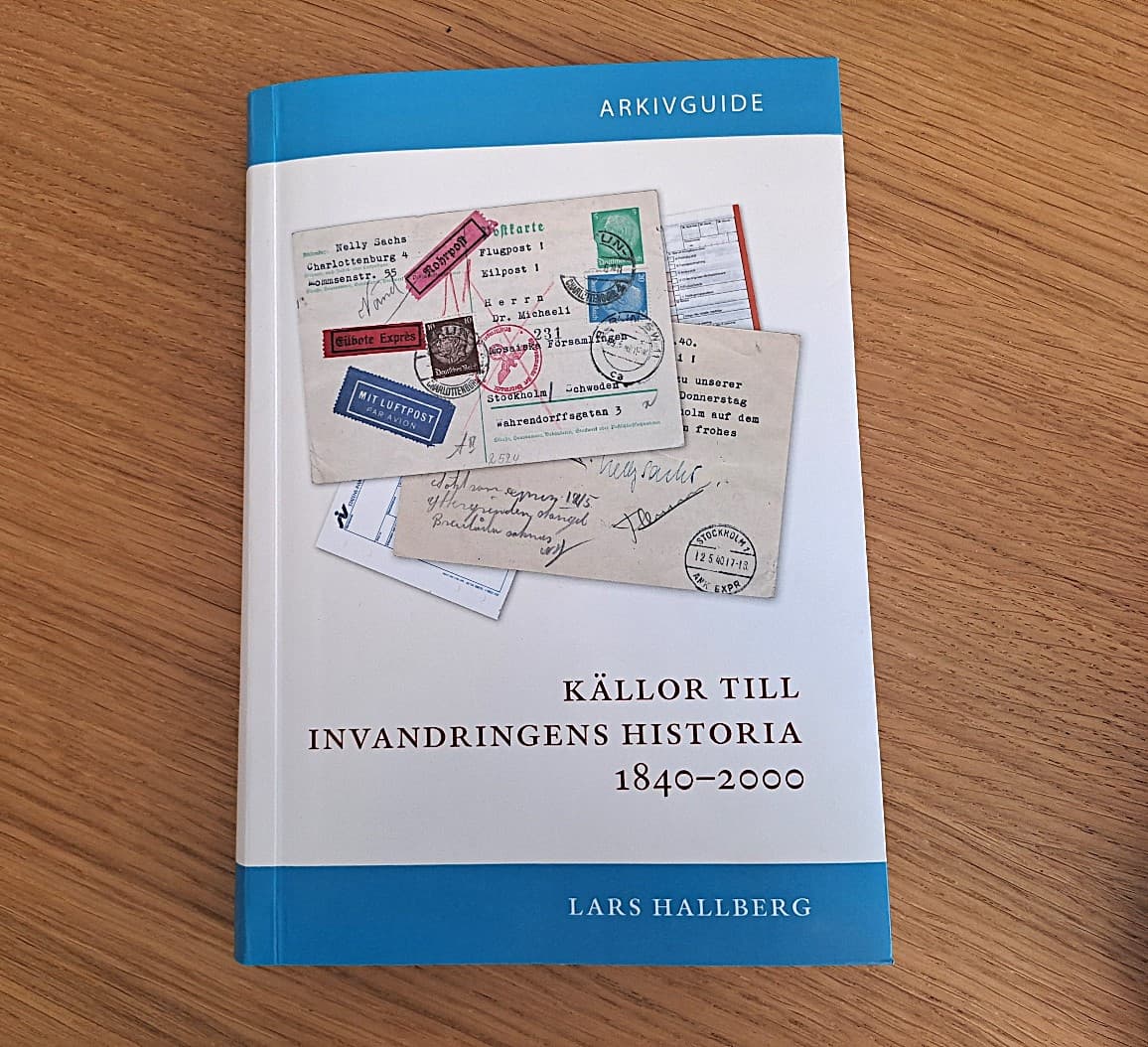 Bok i blått och vitt med titeln Källor till invandringens historia 1840–2000 av författaren Lars Hallberg på ett bord.